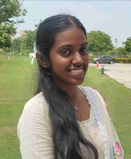 Headshot of Muthameena smiling outside with blue sky and trees and grass in the background.